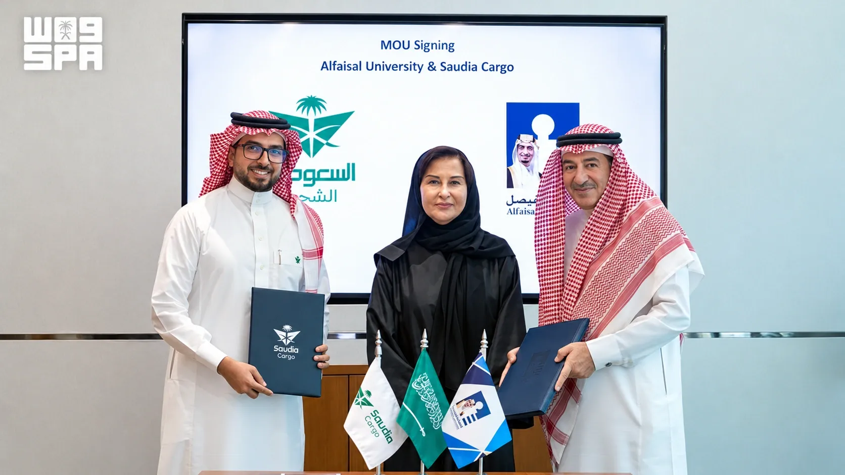Saudia Cargo and Alfaisal University representatives holding signed agreements in front of a screen